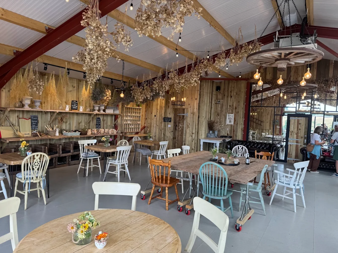 Wooden tables and mismatched chairs beneath hanging dried flowers in the Flower Barn