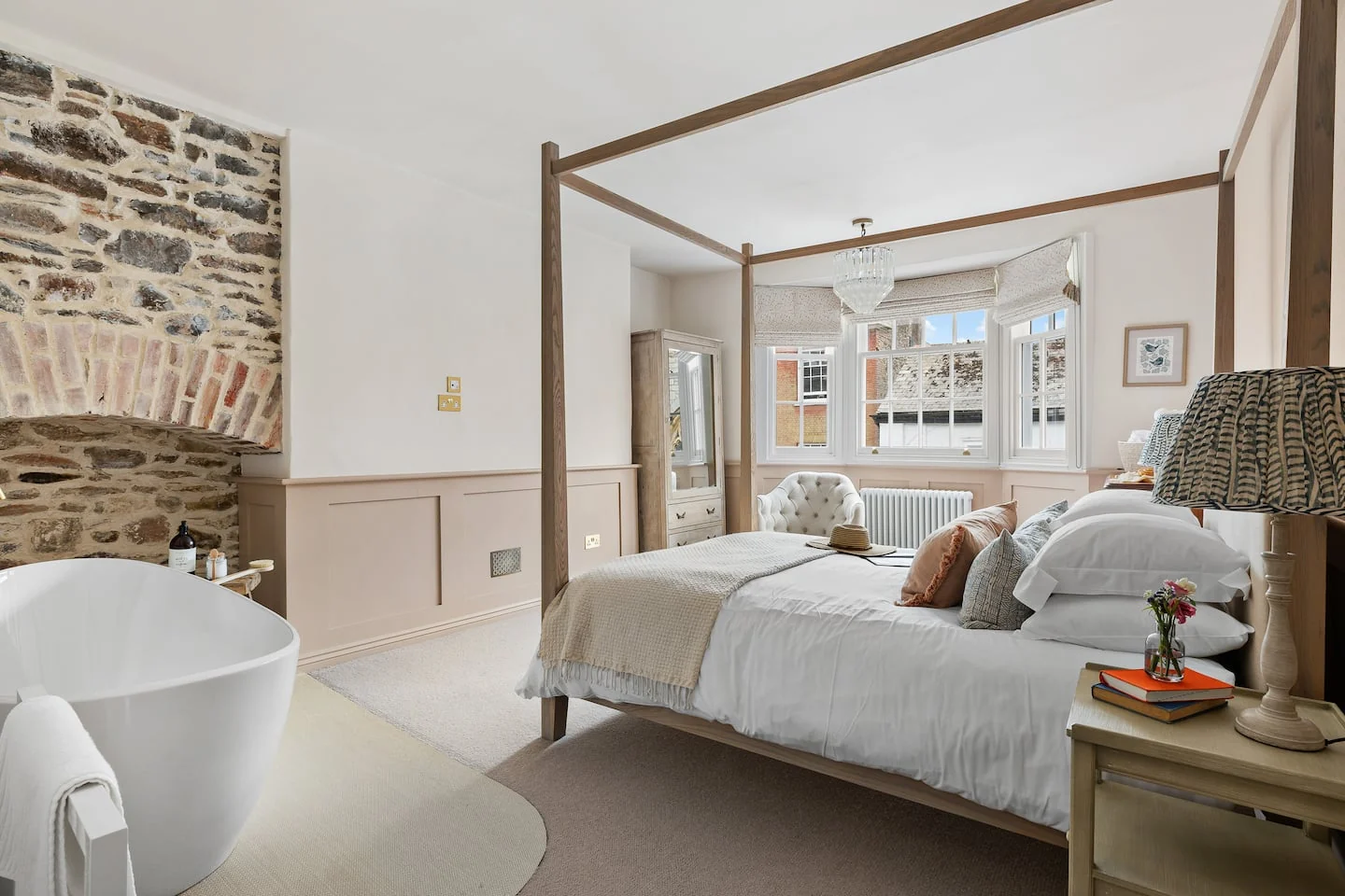 Four-poster bed beside a freestanding bath and exposed stone fireplace