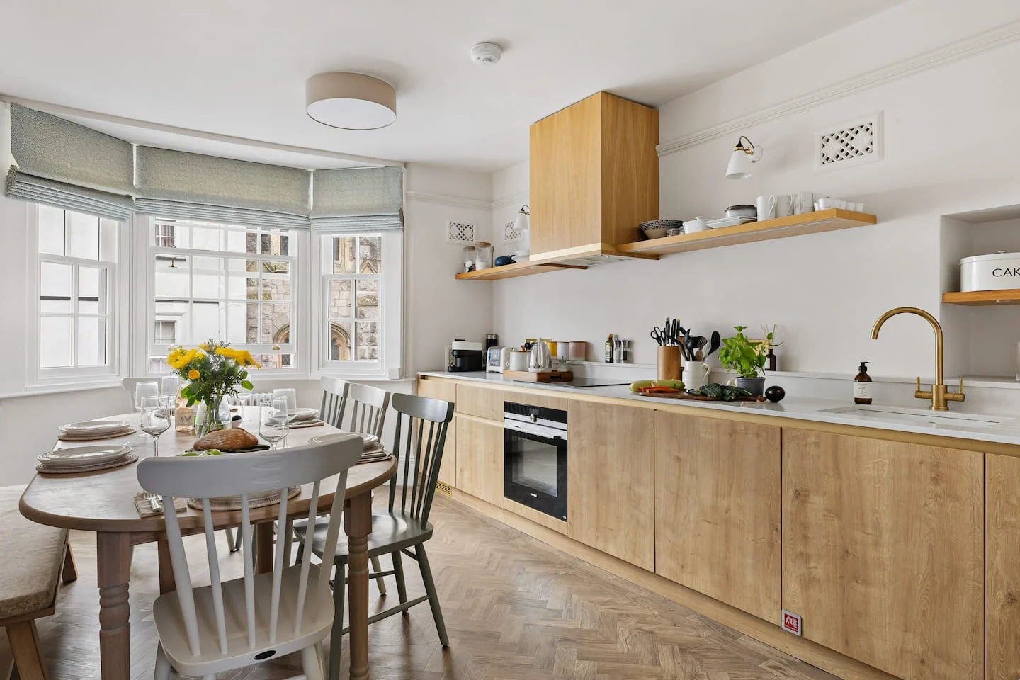 Light wooden kitchen with a dining table beside a bay window