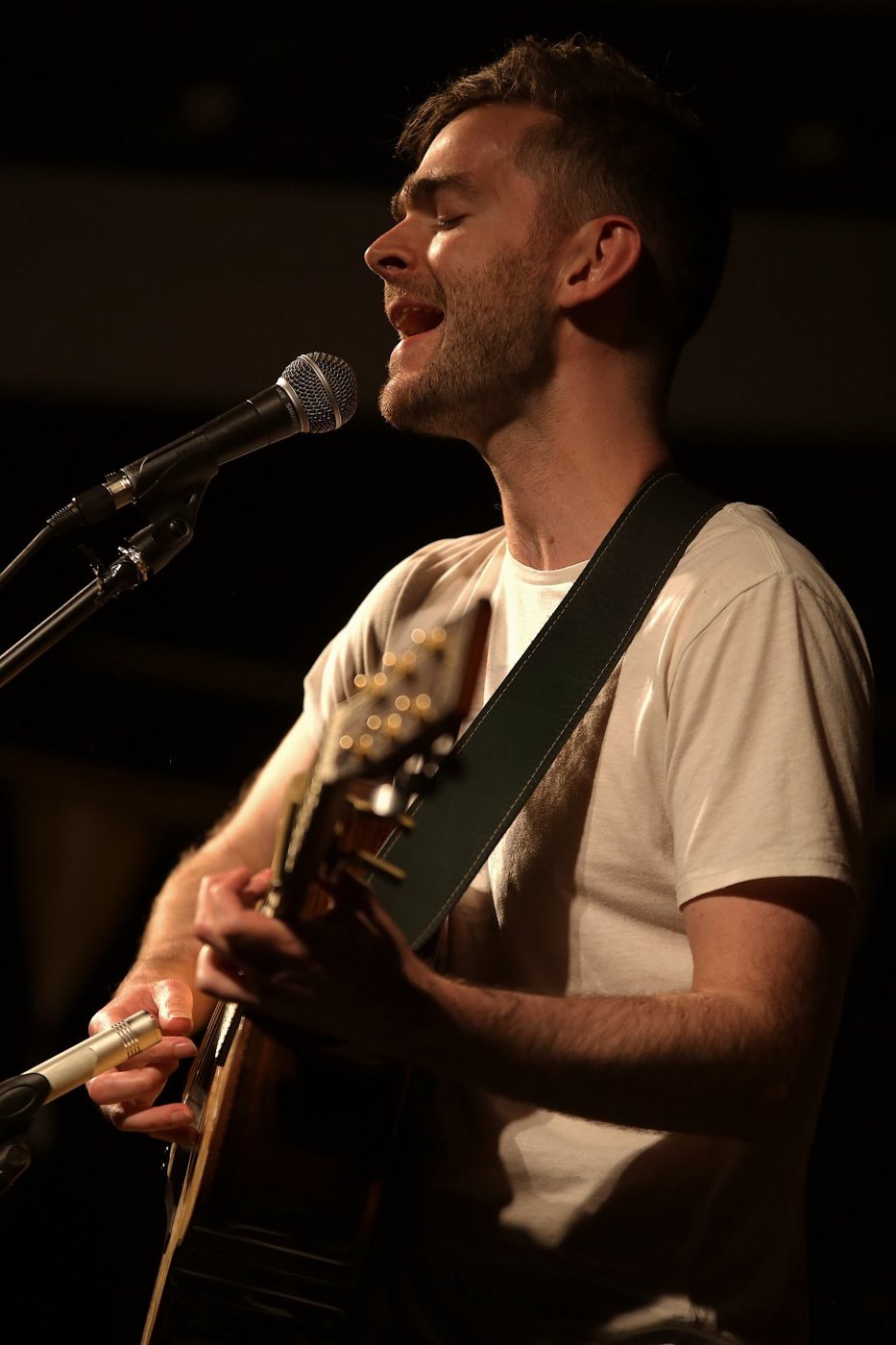 Chris Cleverley singing and playing an acoustic guitar under warm stage lights