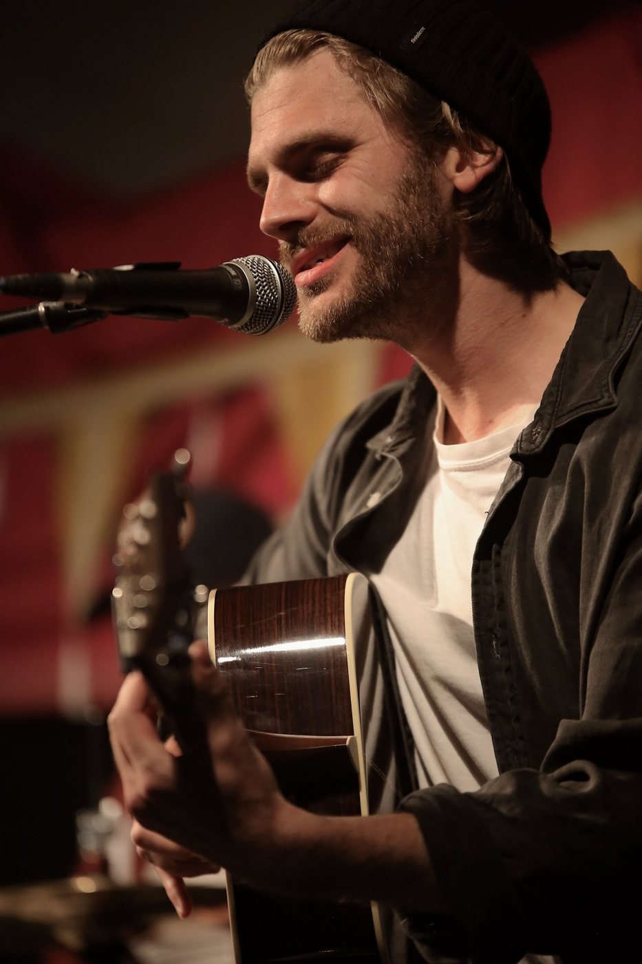 Ollie Dixon singing into a microphone with a guitar and colourful stage backdrop