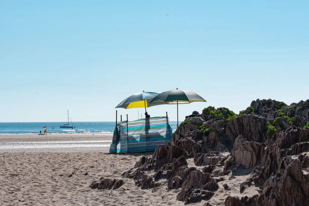 A colourful windbreak and parasol beside rocks on Bantham Beach