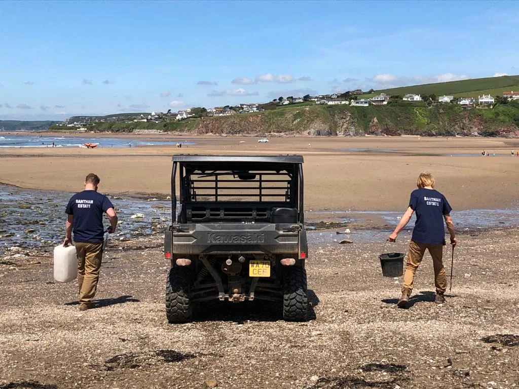 Estate workers carrying buckets beside a utility vehicle on Bantham Beach