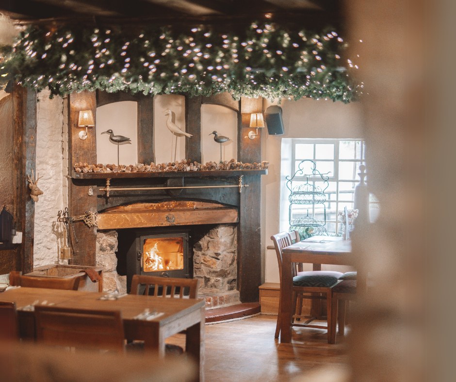 Wood-burning stove beneath a stone fireplace and festive greenery in Bickley Mill Inn