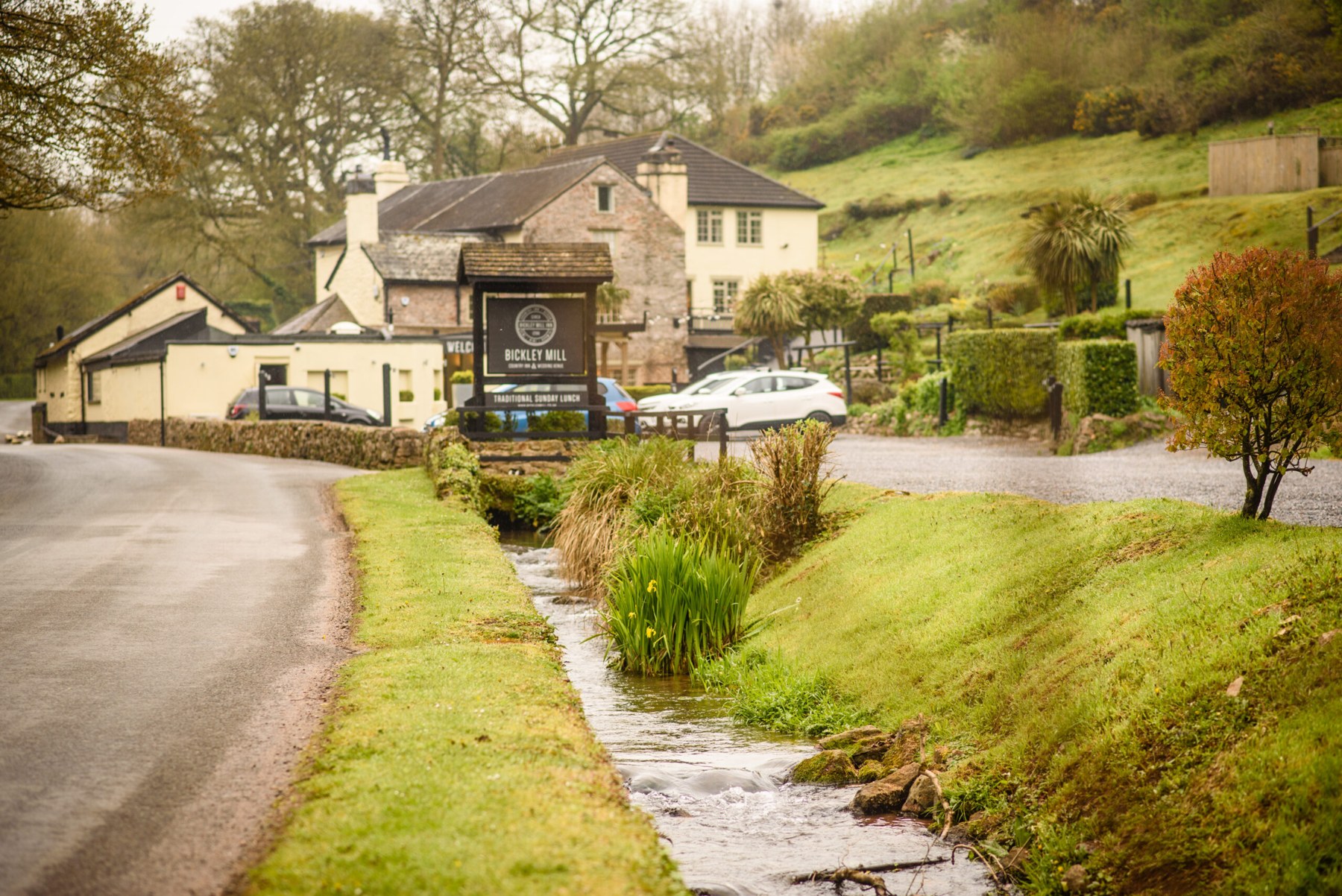 Bickley Mill Inn beside its stream, with green hills rising behind the buildings