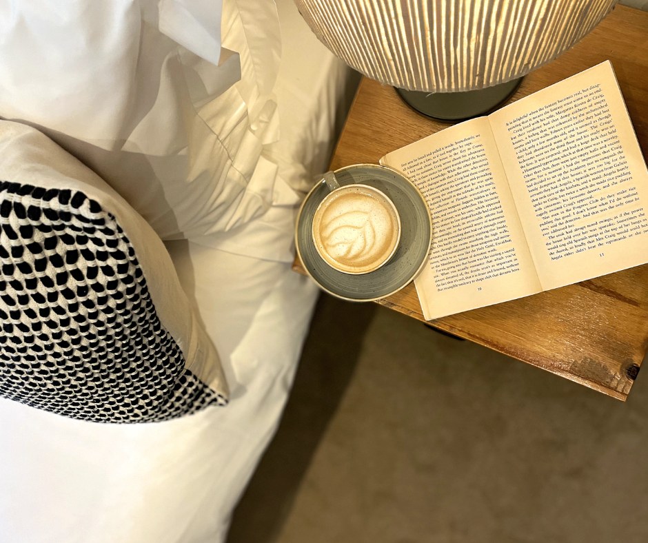 Coffee and an open book beside a bed and lamp at Bickley Mill Inn