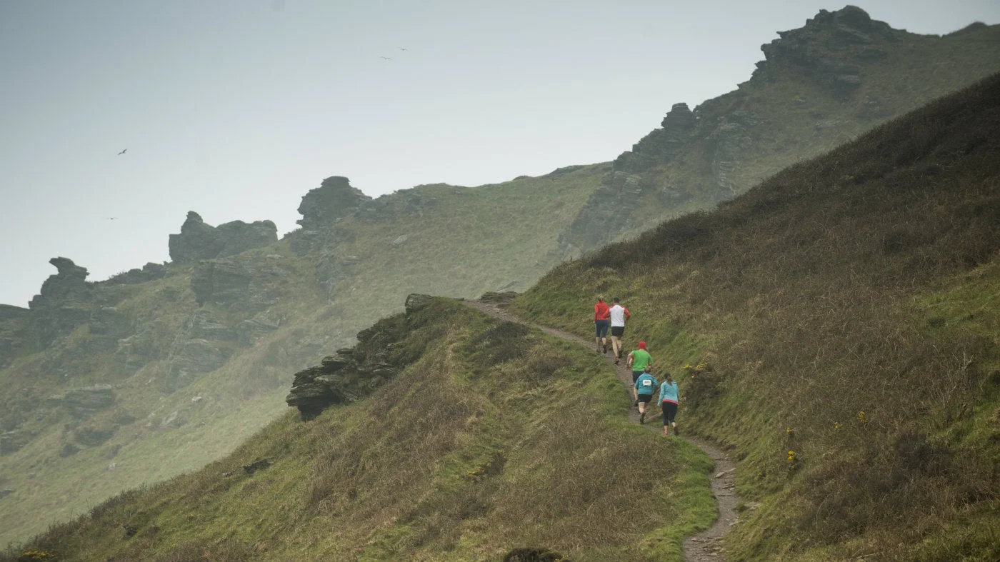 Runners following a grassy coastal path near Bolberry Down