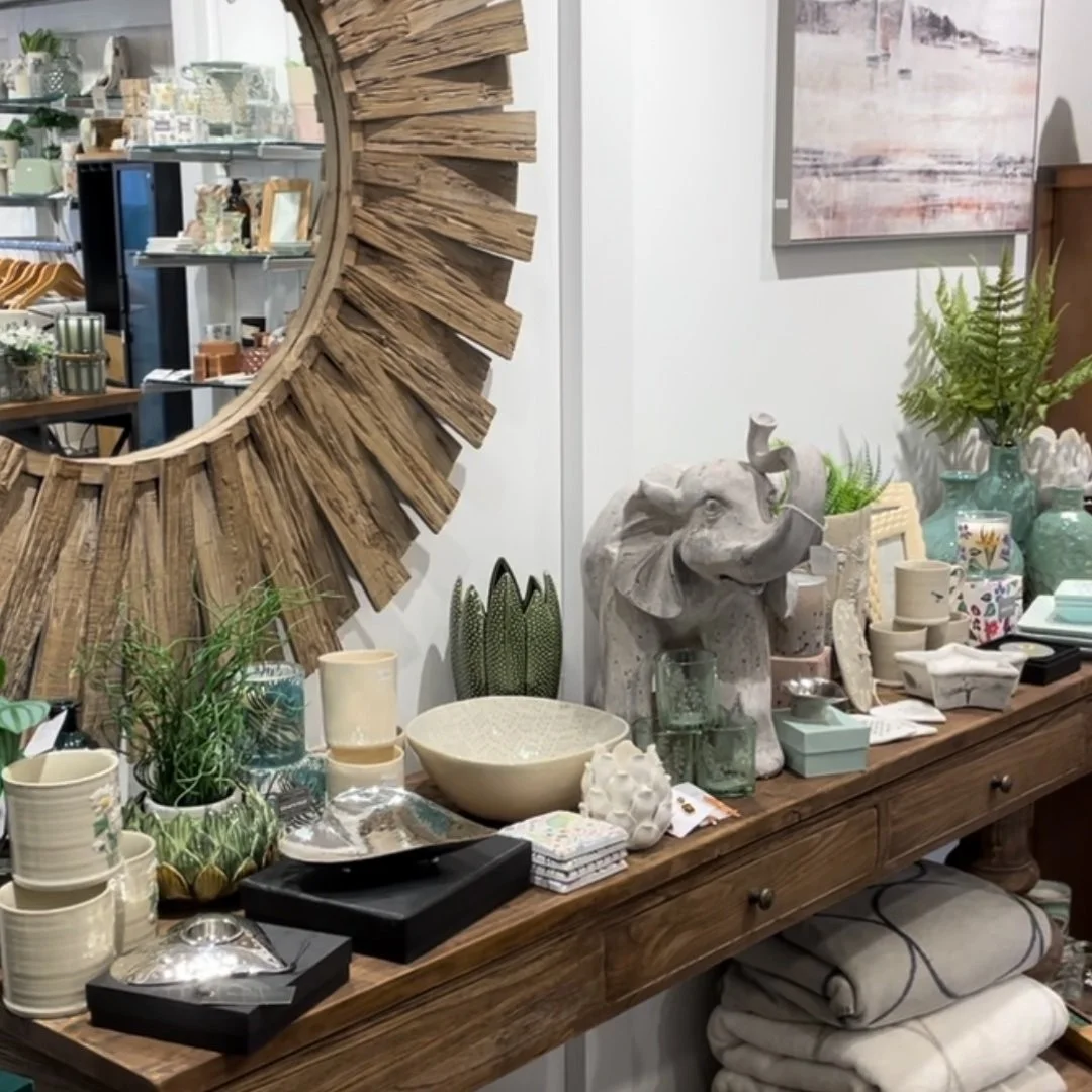 Round decorative mirror above a console of ceramics and gifts