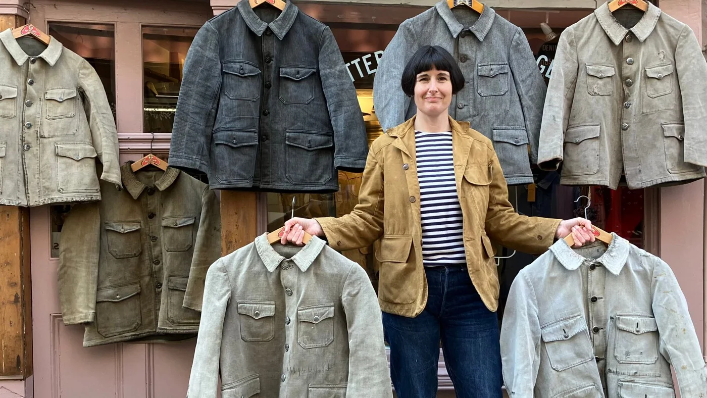 A vintage dealer holding jackets beneath a display of workwear