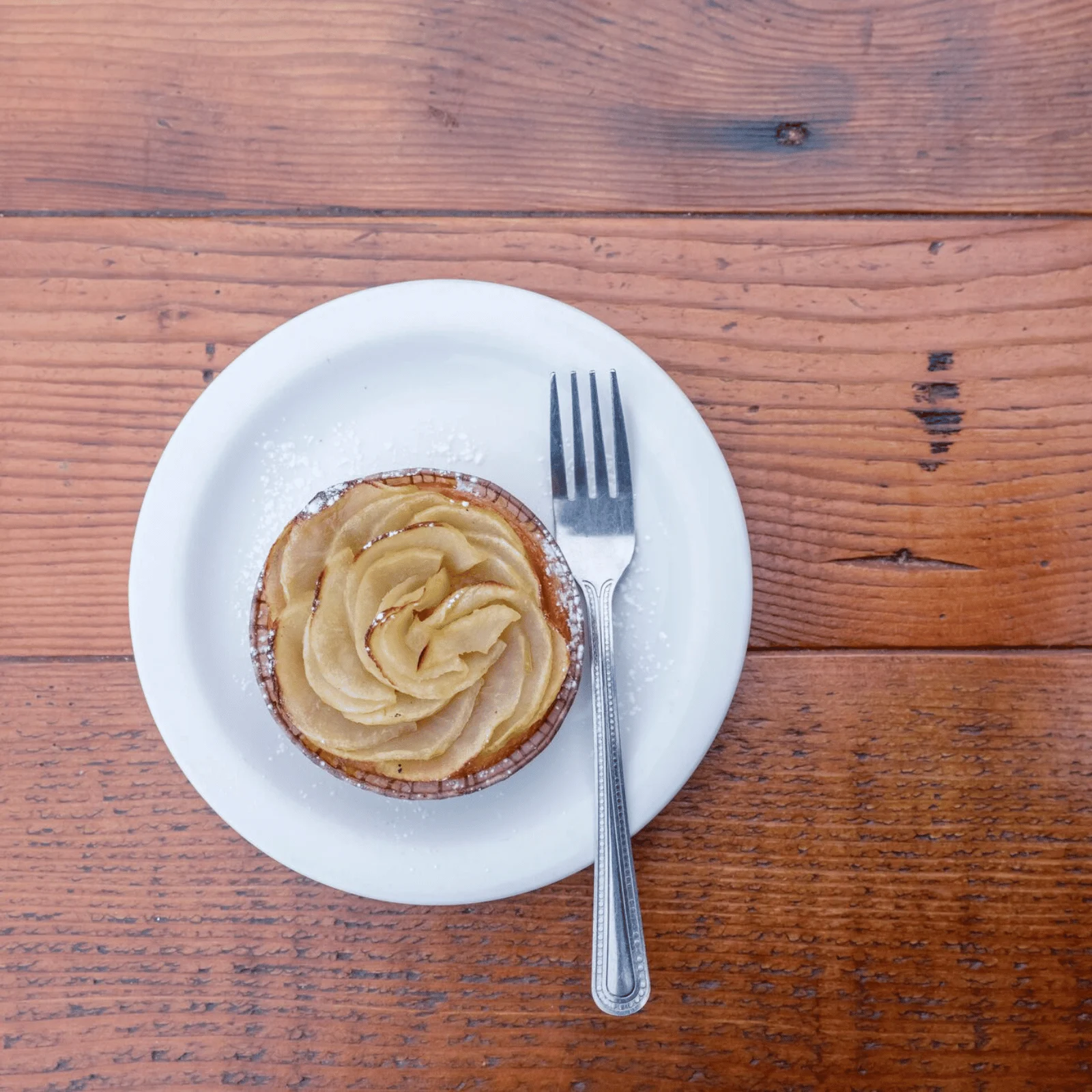 A small apple tart served on a white plate on a wooden table