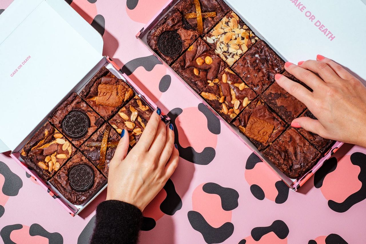 Hands choosing assorted brownies from two pink boxes
