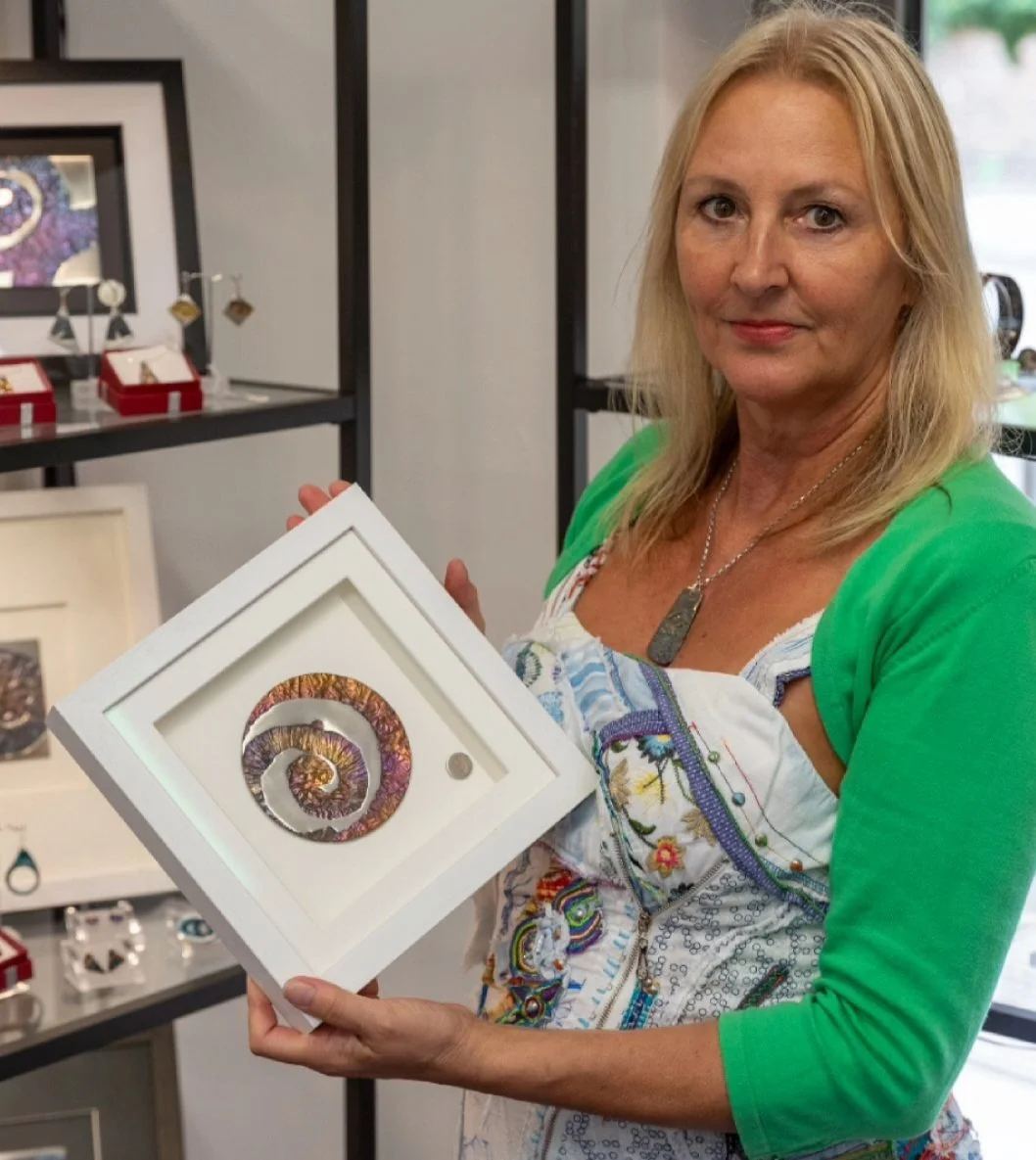 Chrystine Jones holding framed metal artwork in her studio