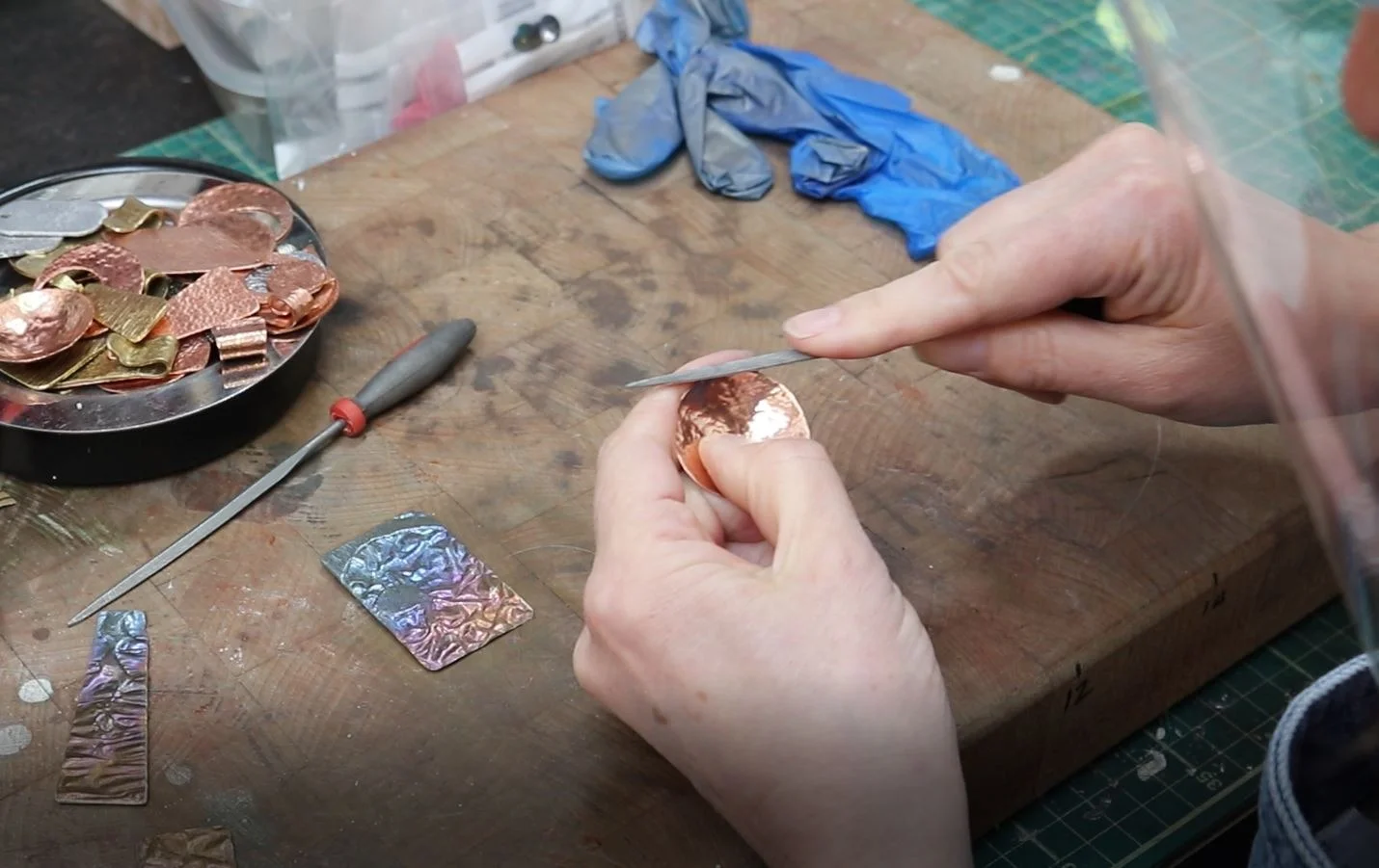 Hands shaping a small piece of metal at a workbench