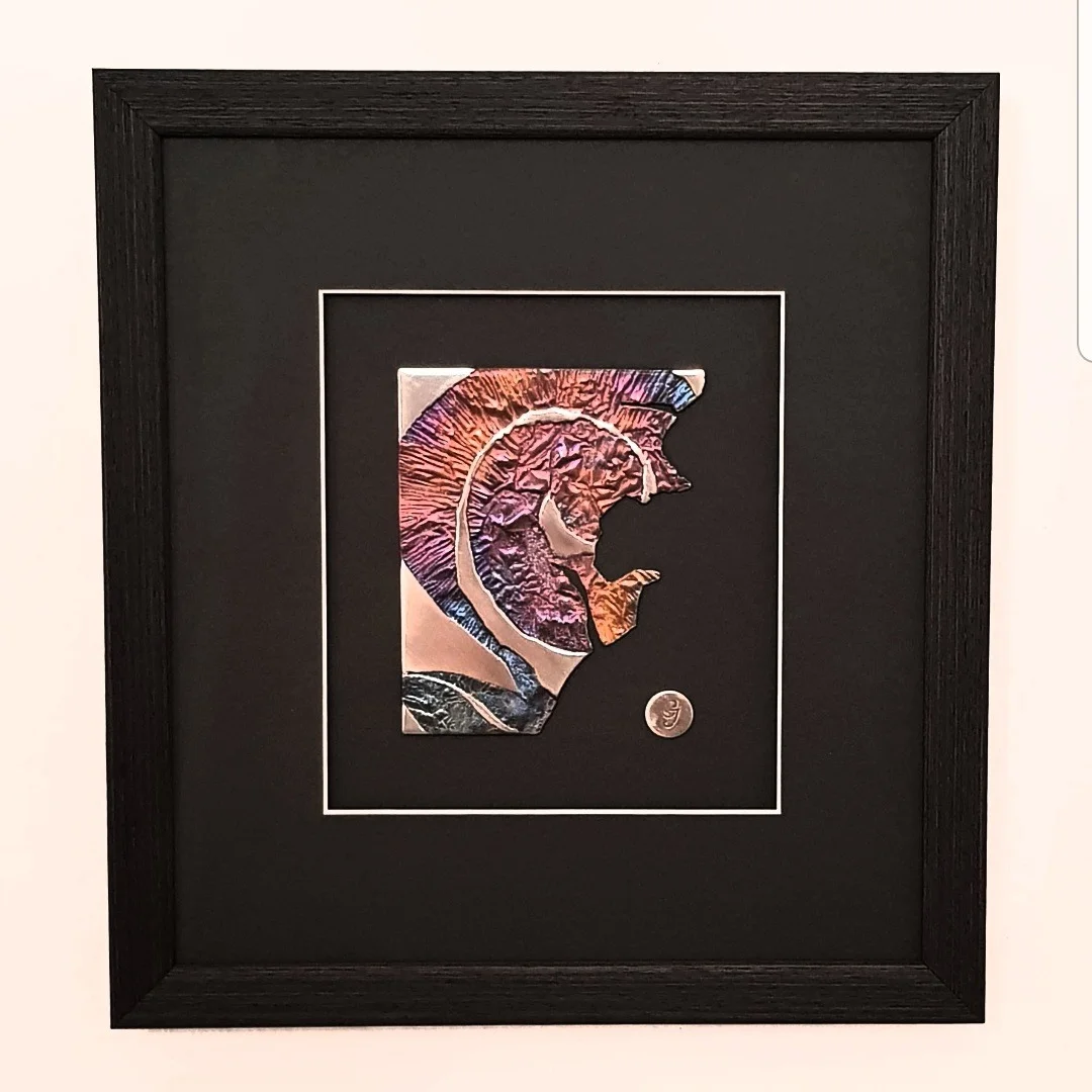 Framed ammonite-shaped metal artwork on a black mount