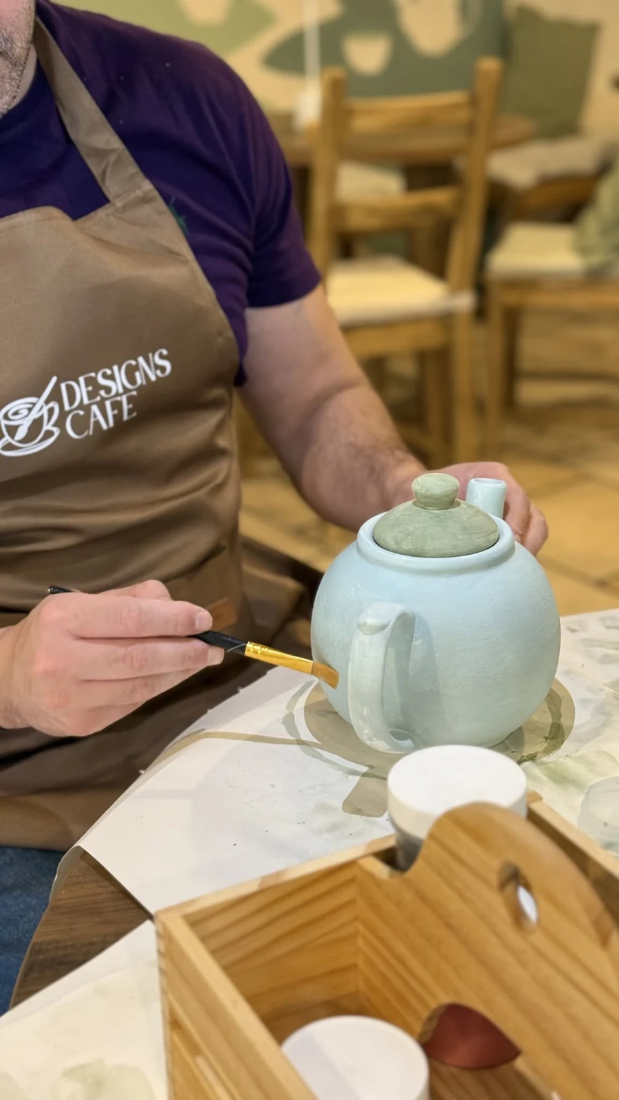 A person painting a pale green teapot at Designs Café