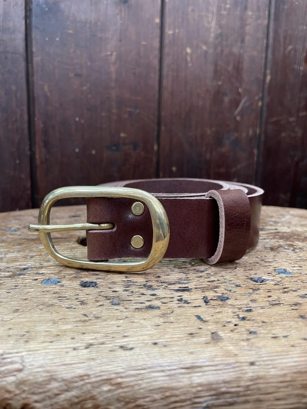 A brown handmade leather belt displayed on wood