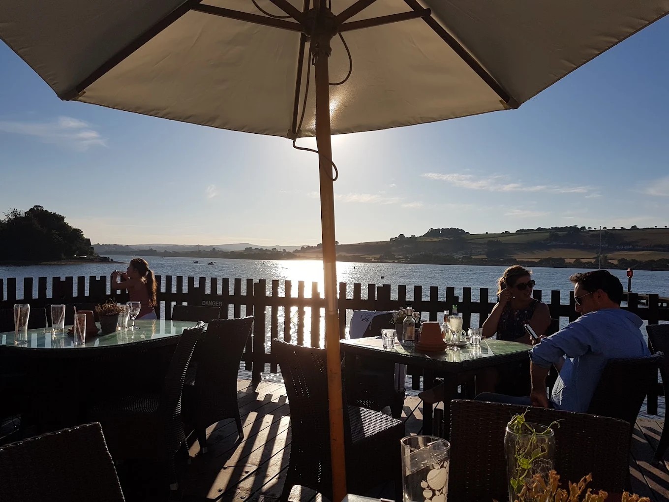 Guests enjoying drinks beneath a parasol on the waterside terrace in evening sunshine