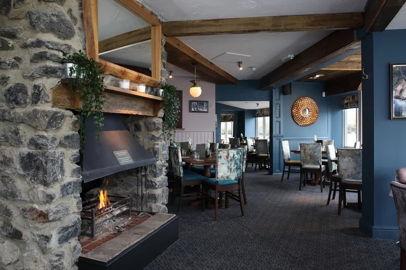 A lit stone fireplace beside dining tables and blue walls at The Coombe Cellars