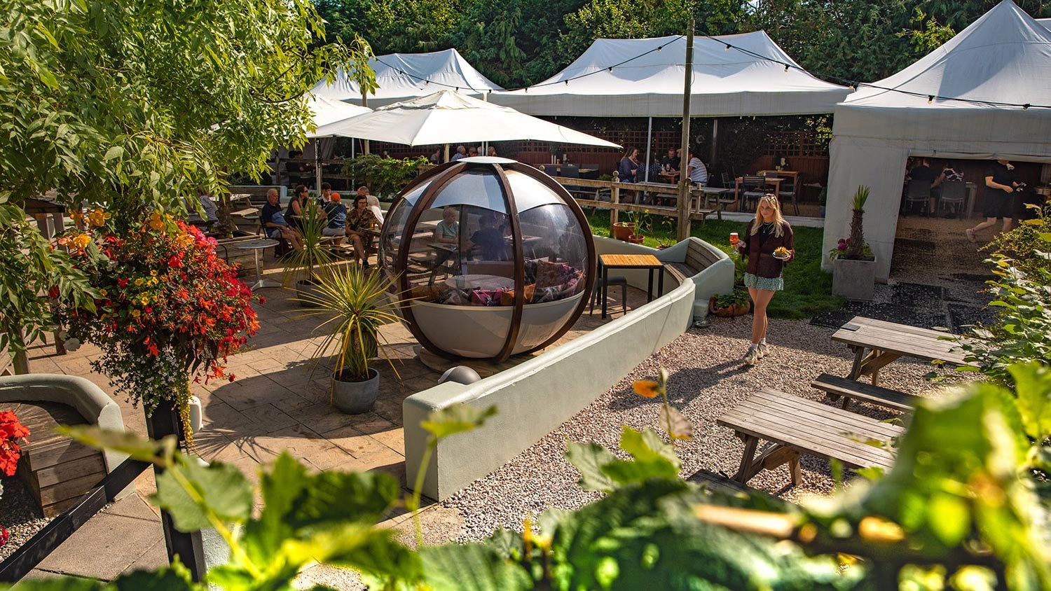 Leafy garden with outdoor dining tables and a transparent dining pod at The Cott Inn