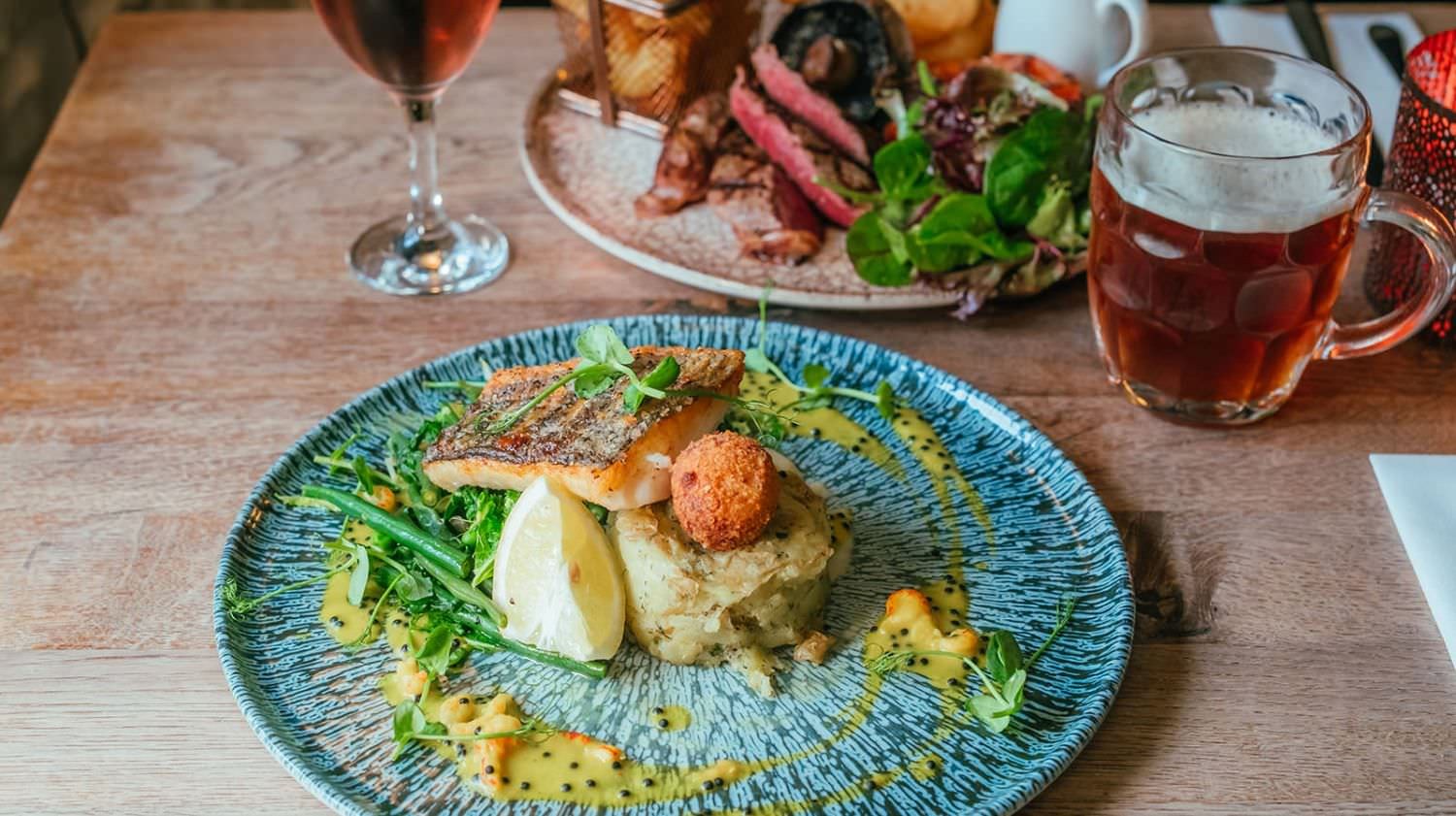 Colourful plates of food and drinks on a wooden table at The Cott Inn