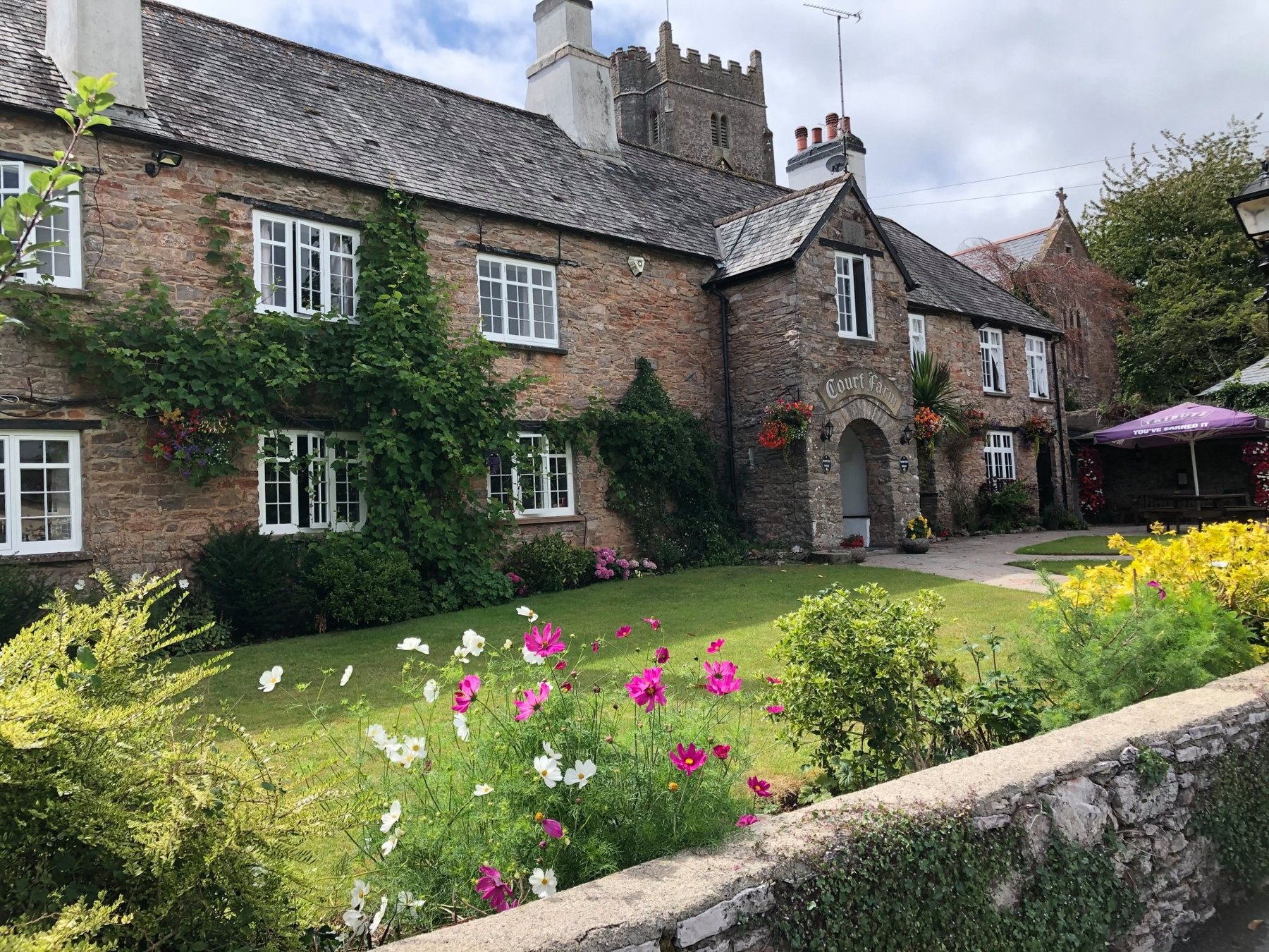 Stone frontage of Court Farm Inn with a lawn and colourful flowers