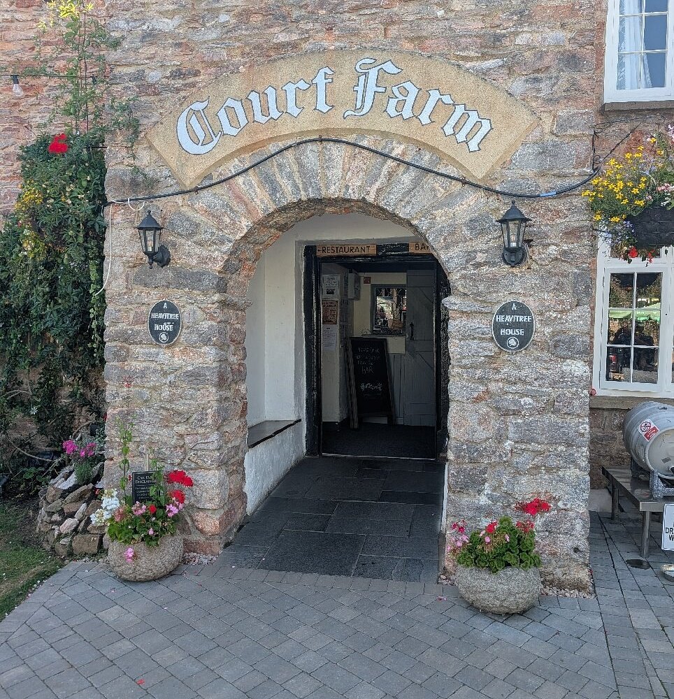 Arched stone entrance to Court Farm Inn framed by flower pots