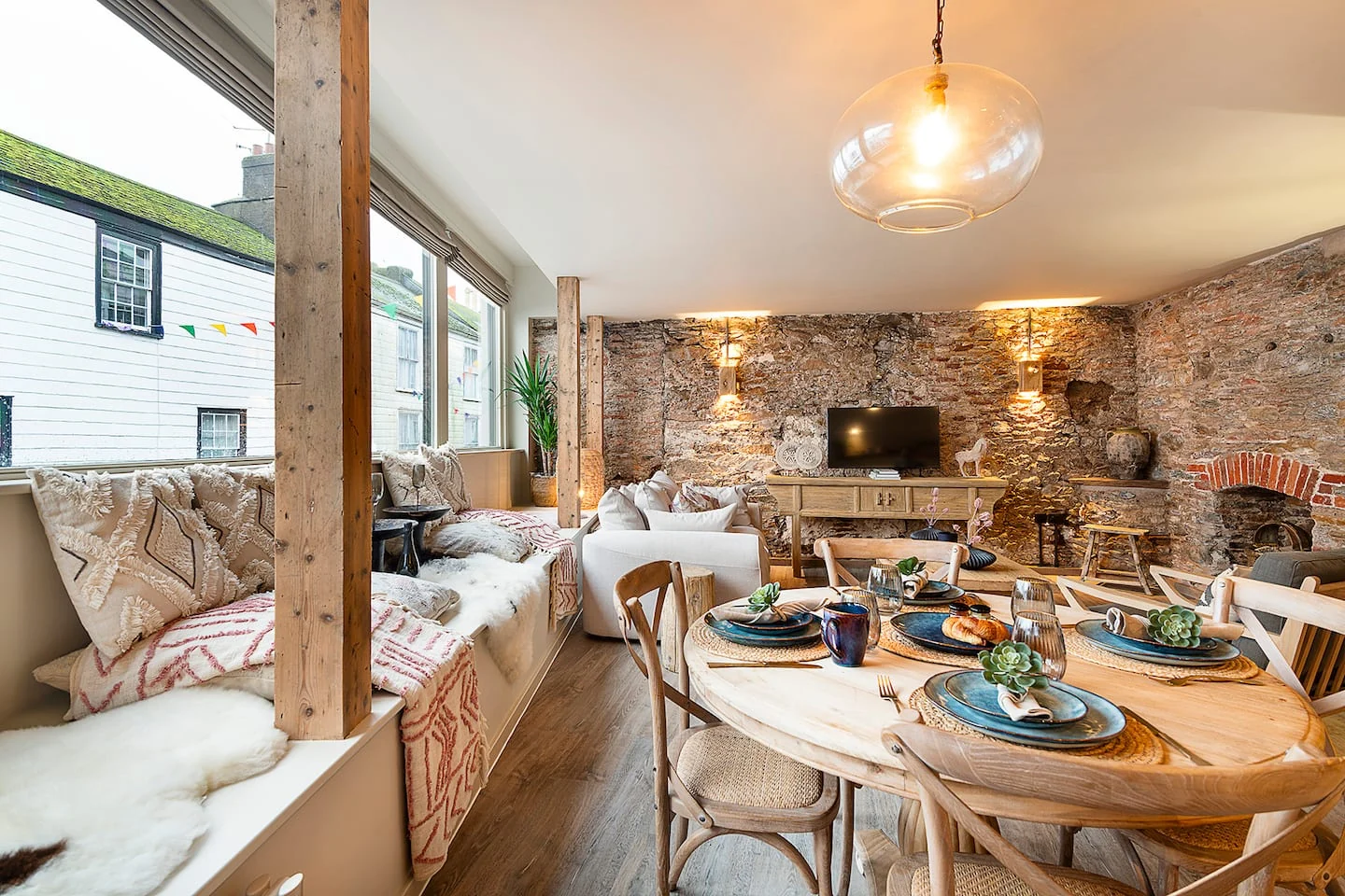 Dining table and cushioned window seats beside an exposed stone wall