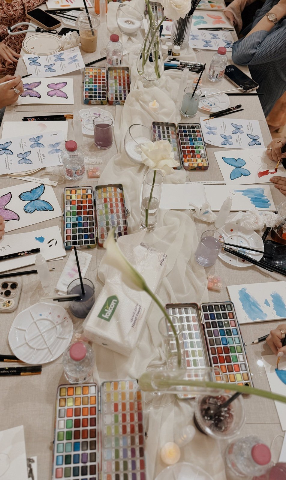 Watercolour paints and botanical paintings spread across a workshop table