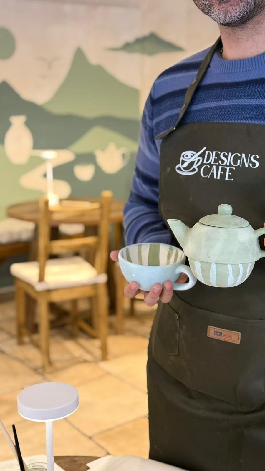 A Designs Café team member holding a green-and-white painted teapot and cup