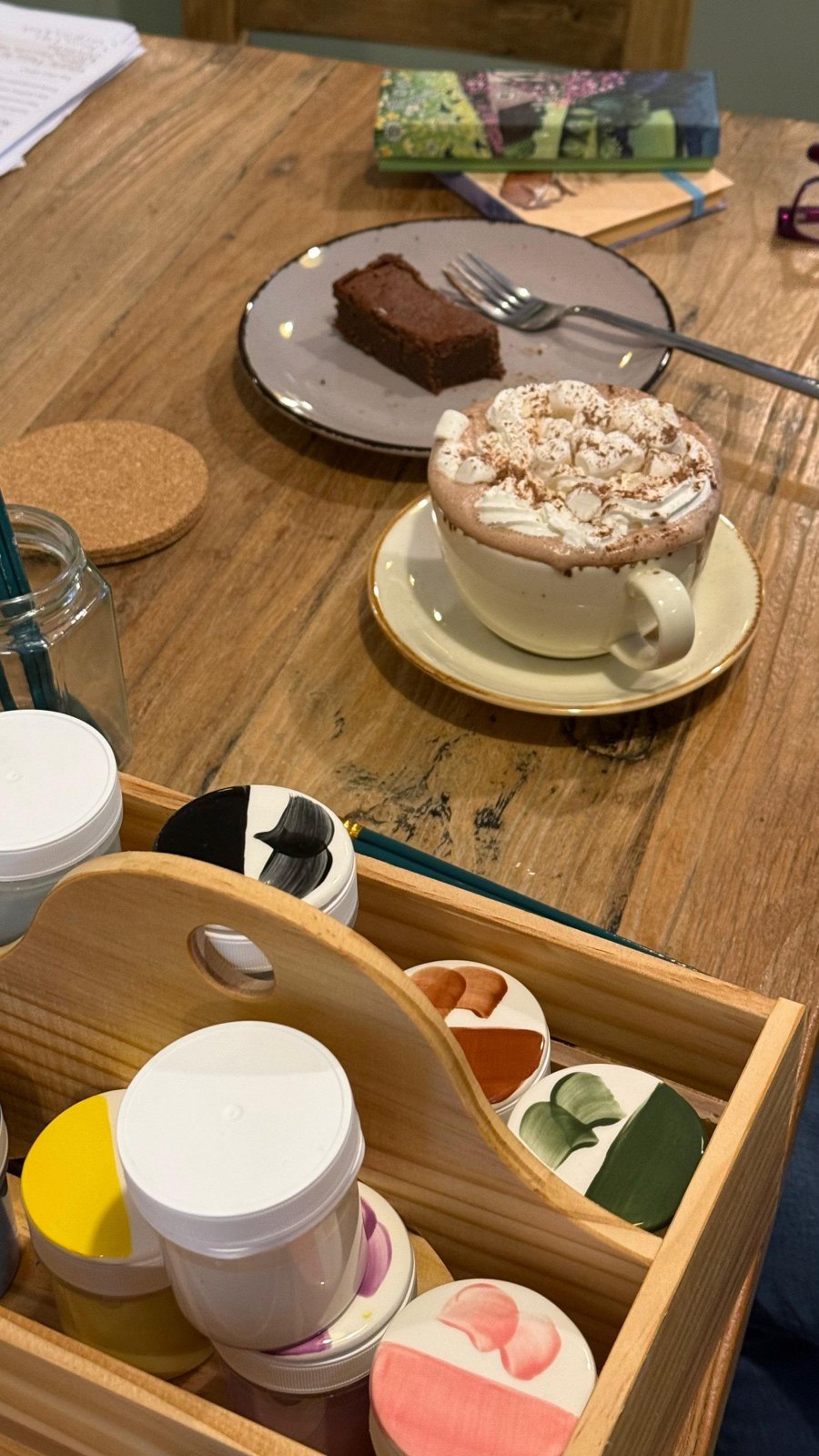 Paints, brushes, cake and hot chocolate on a table at Designs Café