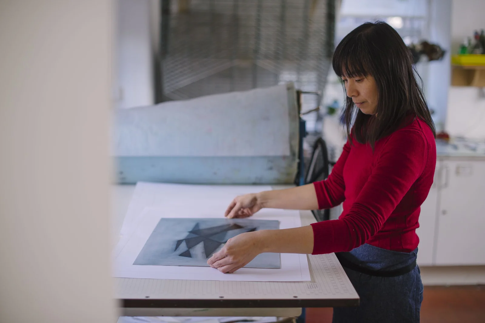 A printmaker placing a sheet of paper on a printing press