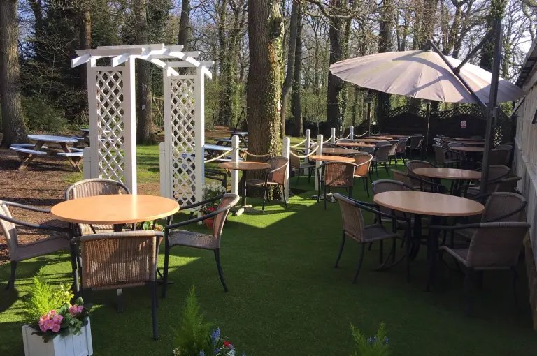 Outdoor café tables beneath a parasol beside trees at Fermoy’s