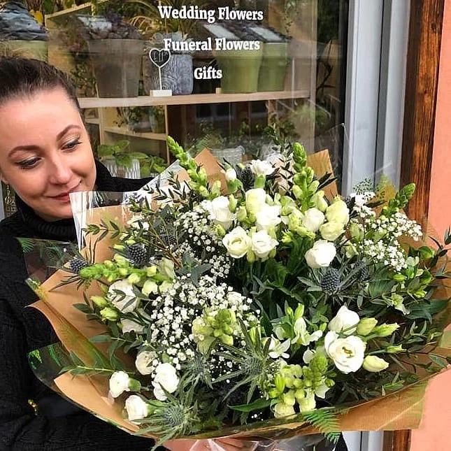 Vita holding a large green and white bouquet outside her studio