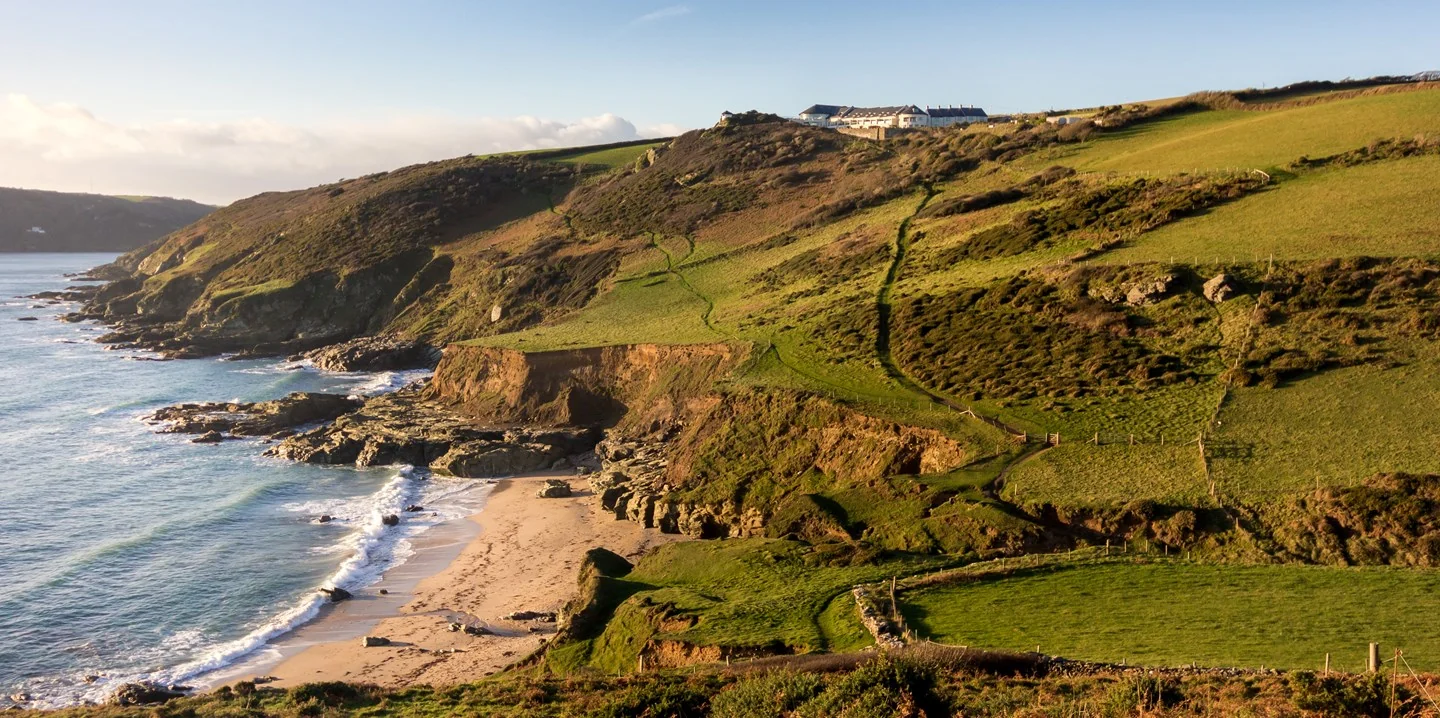 Rocky shoreline and sandy cove below green coastal slopes