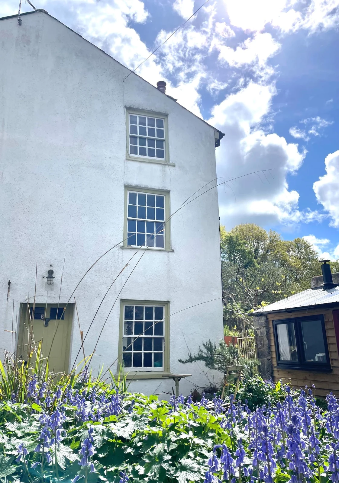 White cottage exterior beside a leafy garden