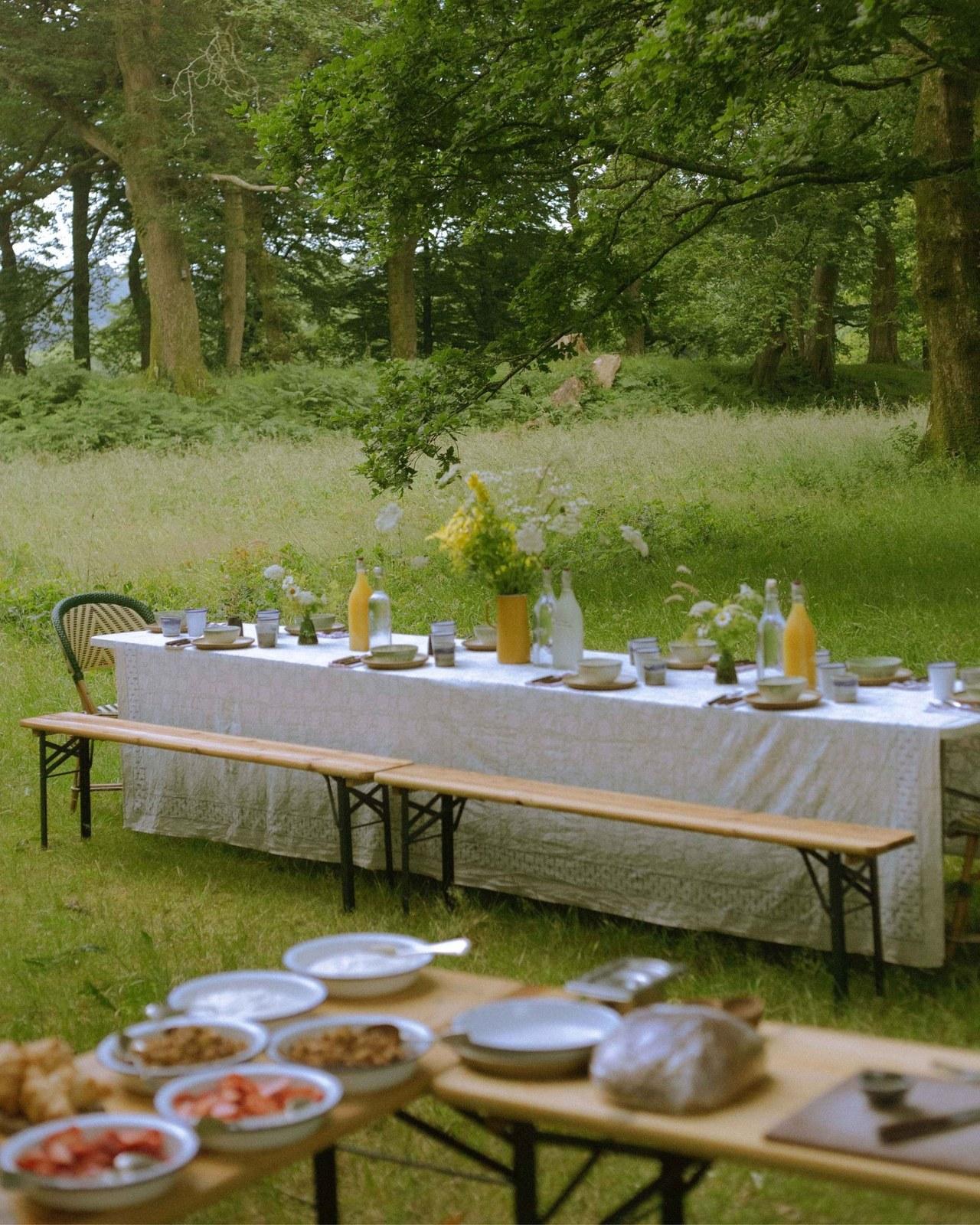 A long breakfast table set beneath trees at Glebe House