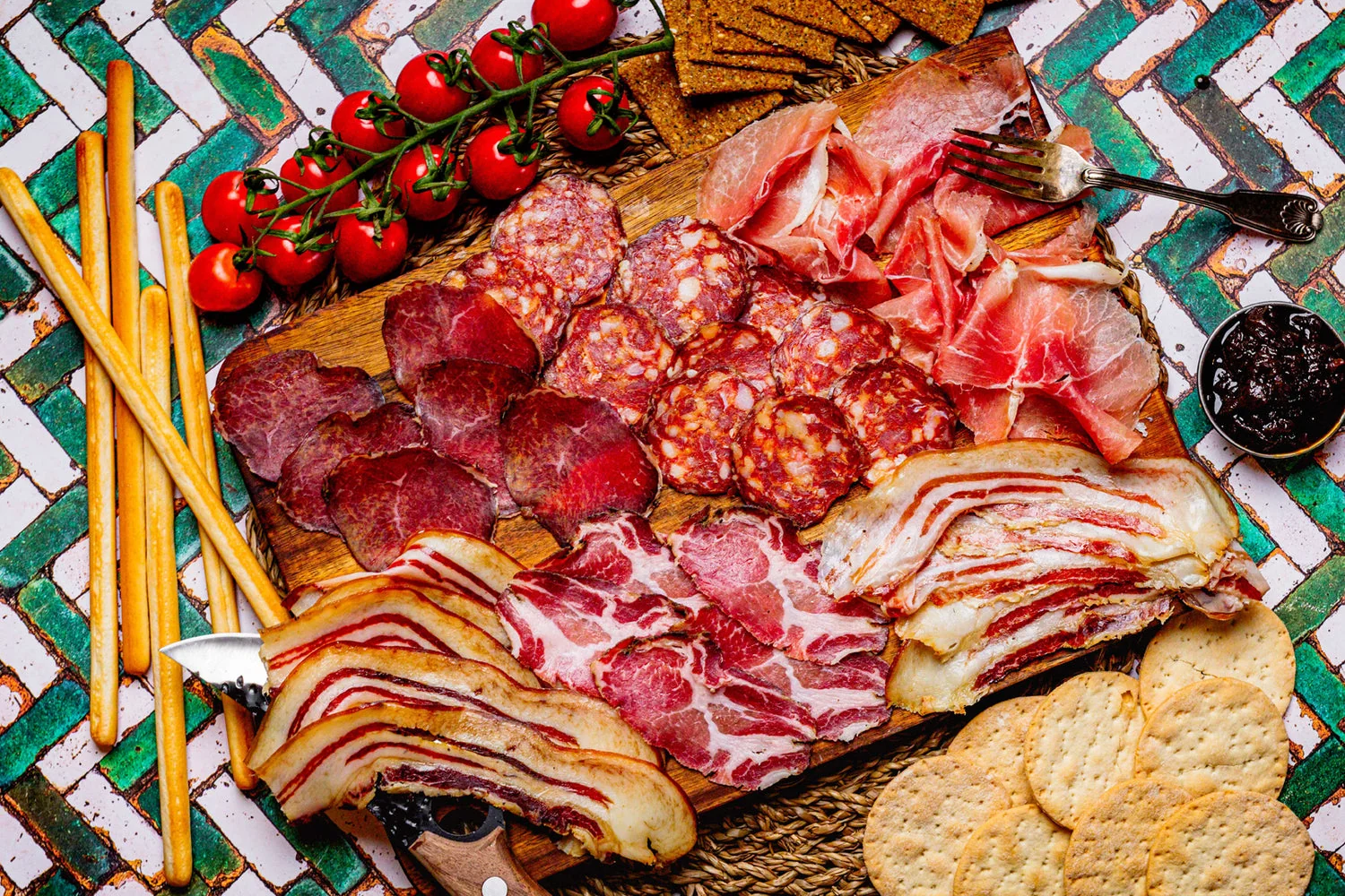 Sharing platter of sliced cured meats with bread and tomatoes