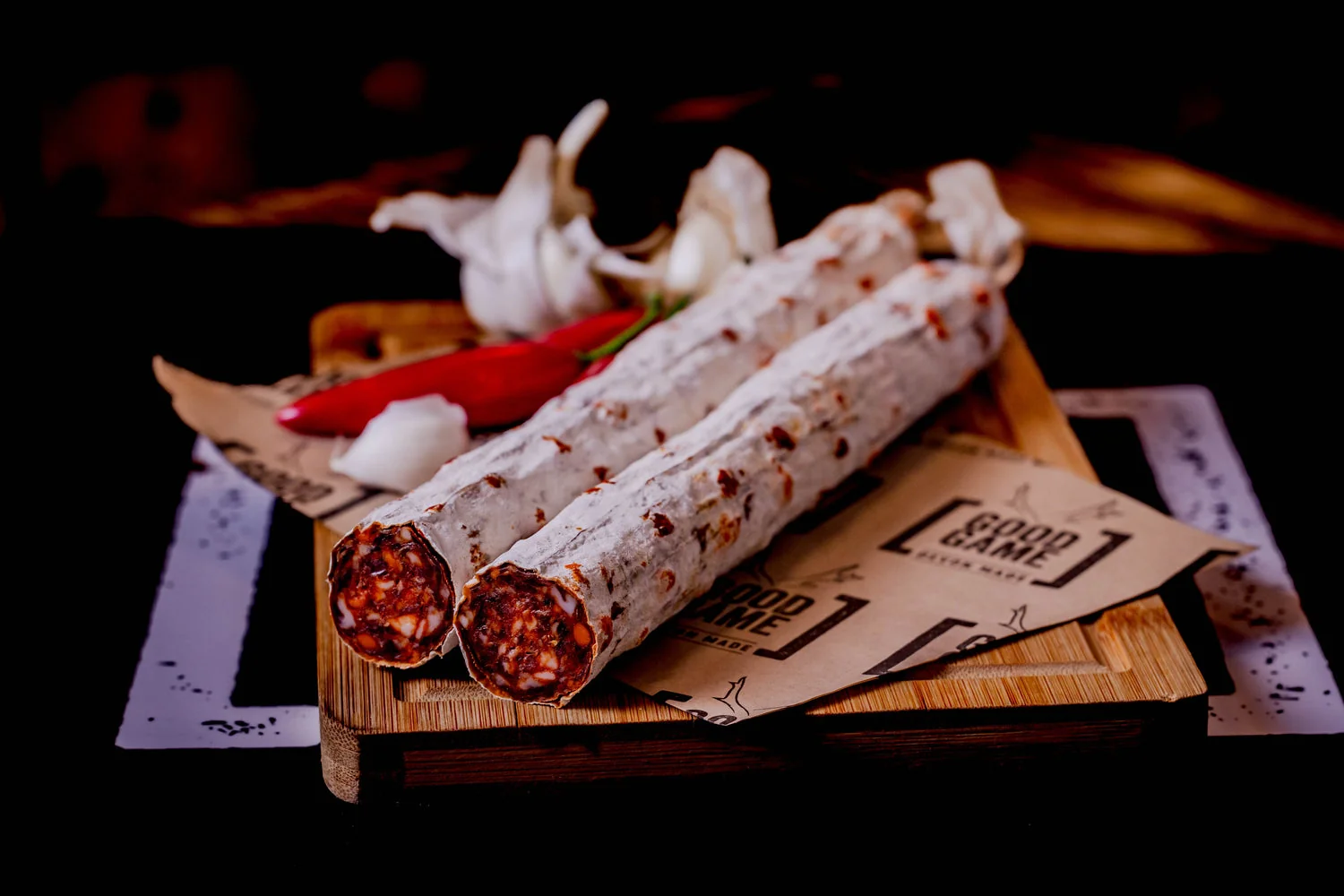Whole cured salami on a board beside sliced vegetables
