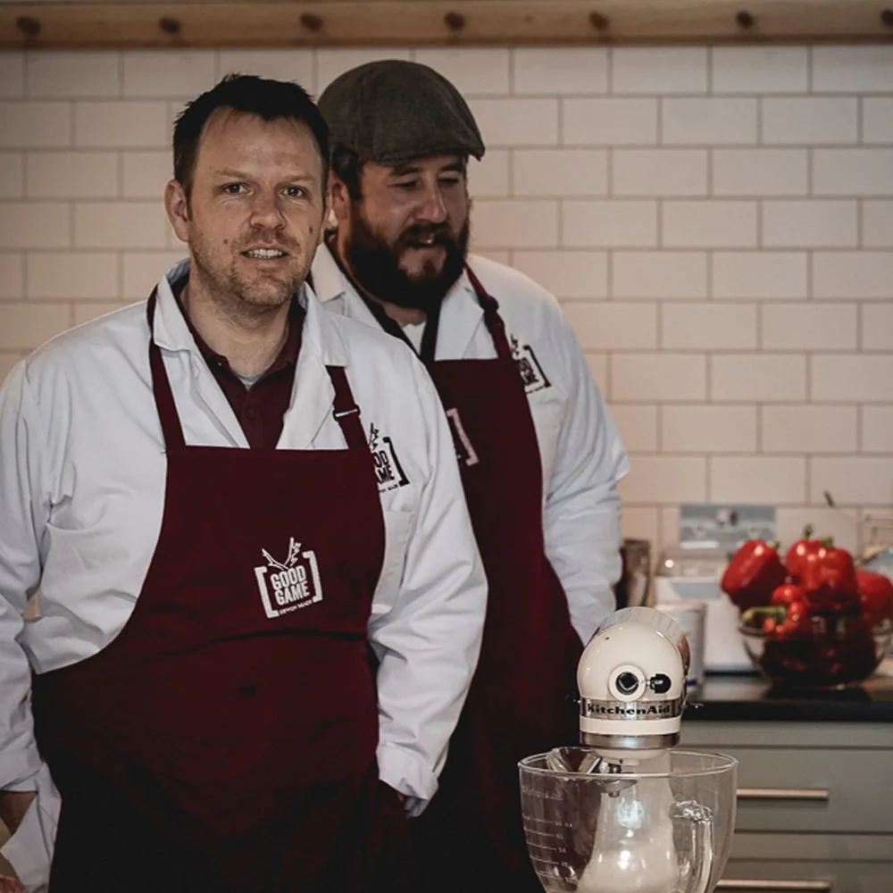 Two Good Game team members in aprons in a tiled workspace