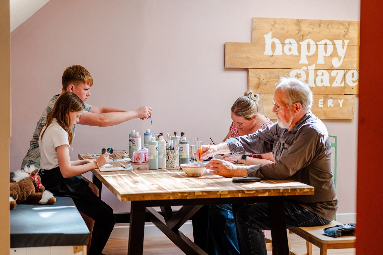 People painting pottery around a table at Happy Glaze