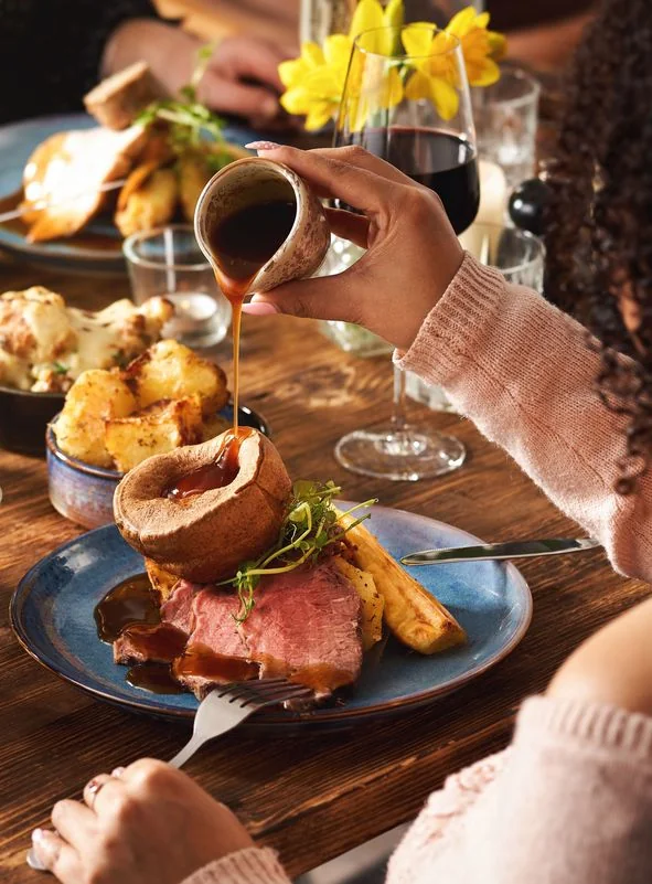 Gravy being poured over a roast dinner with Yorkshire pudding