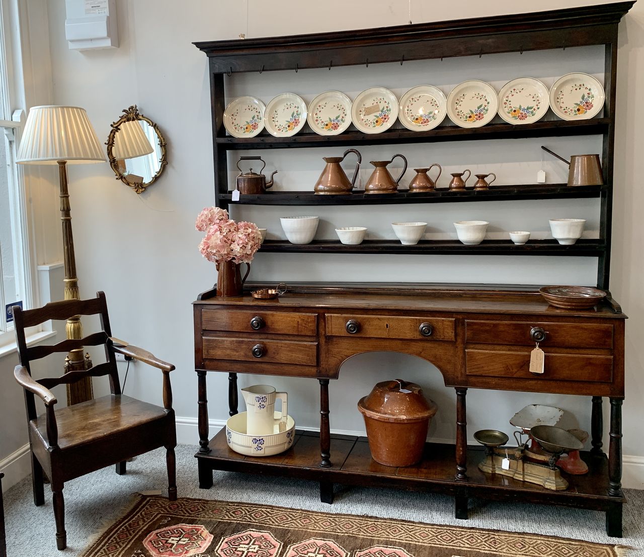 An antique dresser displaying plates and cups, with a wooden chair alongside