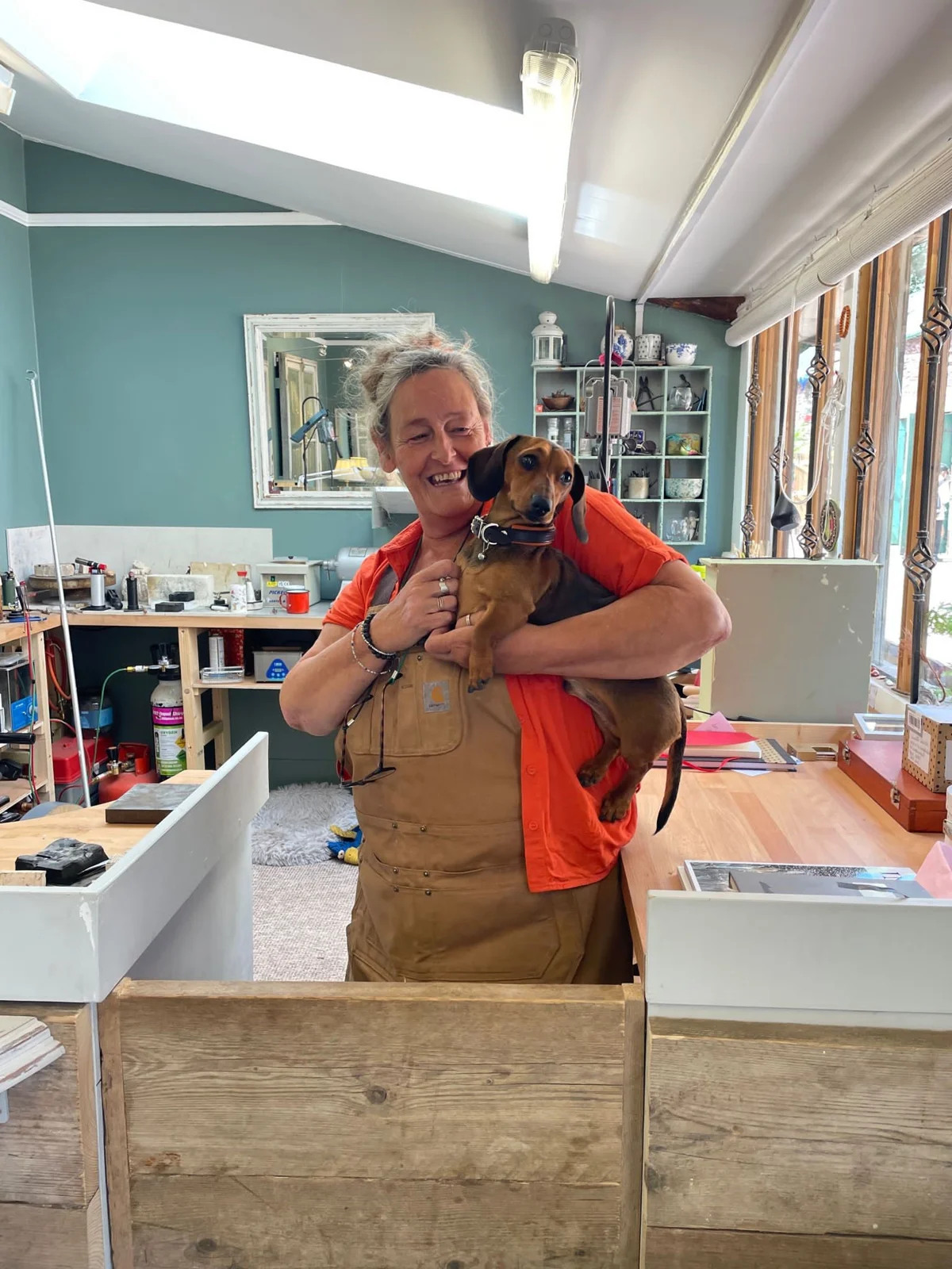 Jo Bradford in her jewellery studio holding a dachshund