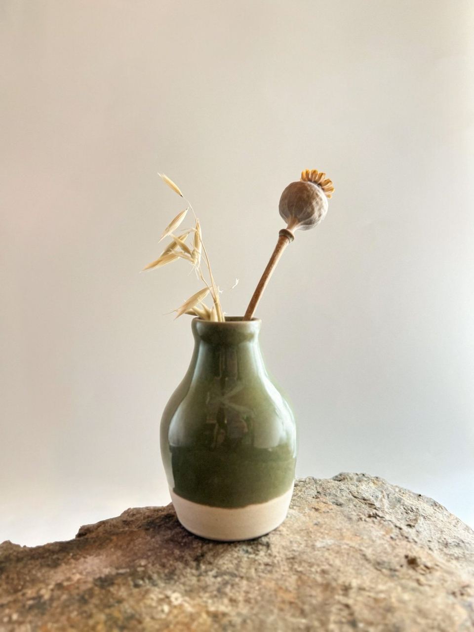 An olive green vase holding dried stems on a stone ledge