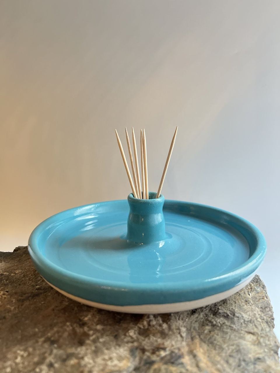A turquoise ceramic incense holder on a stone surface