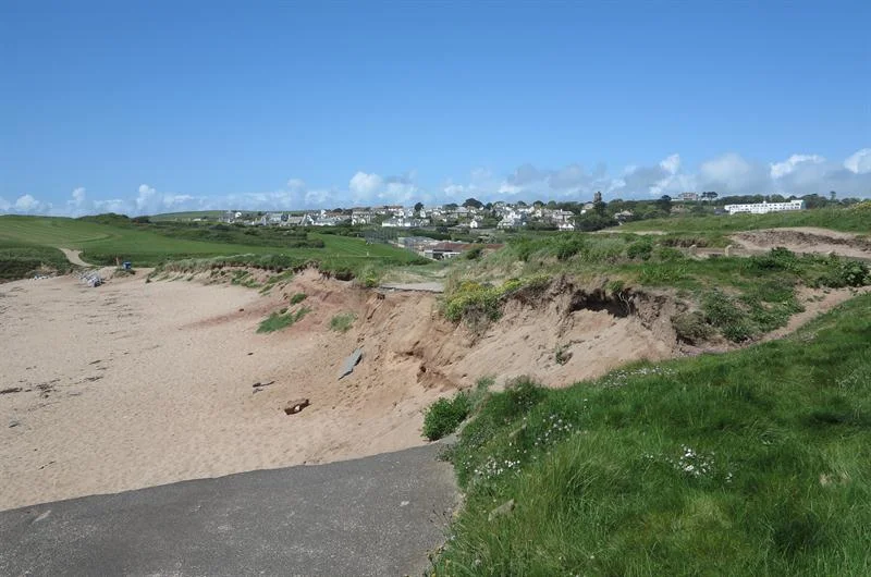 Paved path descending through grass towards the sandy beach