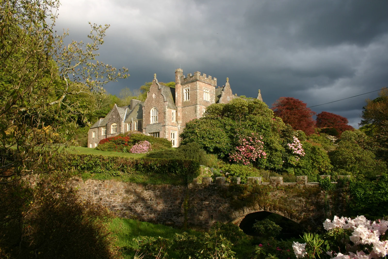 Lukesland House and a garden bridge beneath dramatic clouds