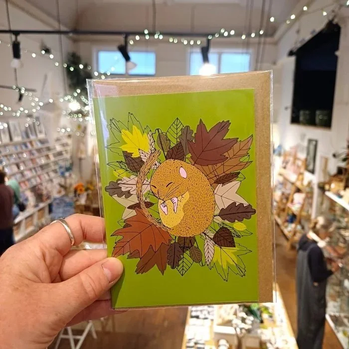 A hand holding an illustrated autumn greetings card inside Maker Mart