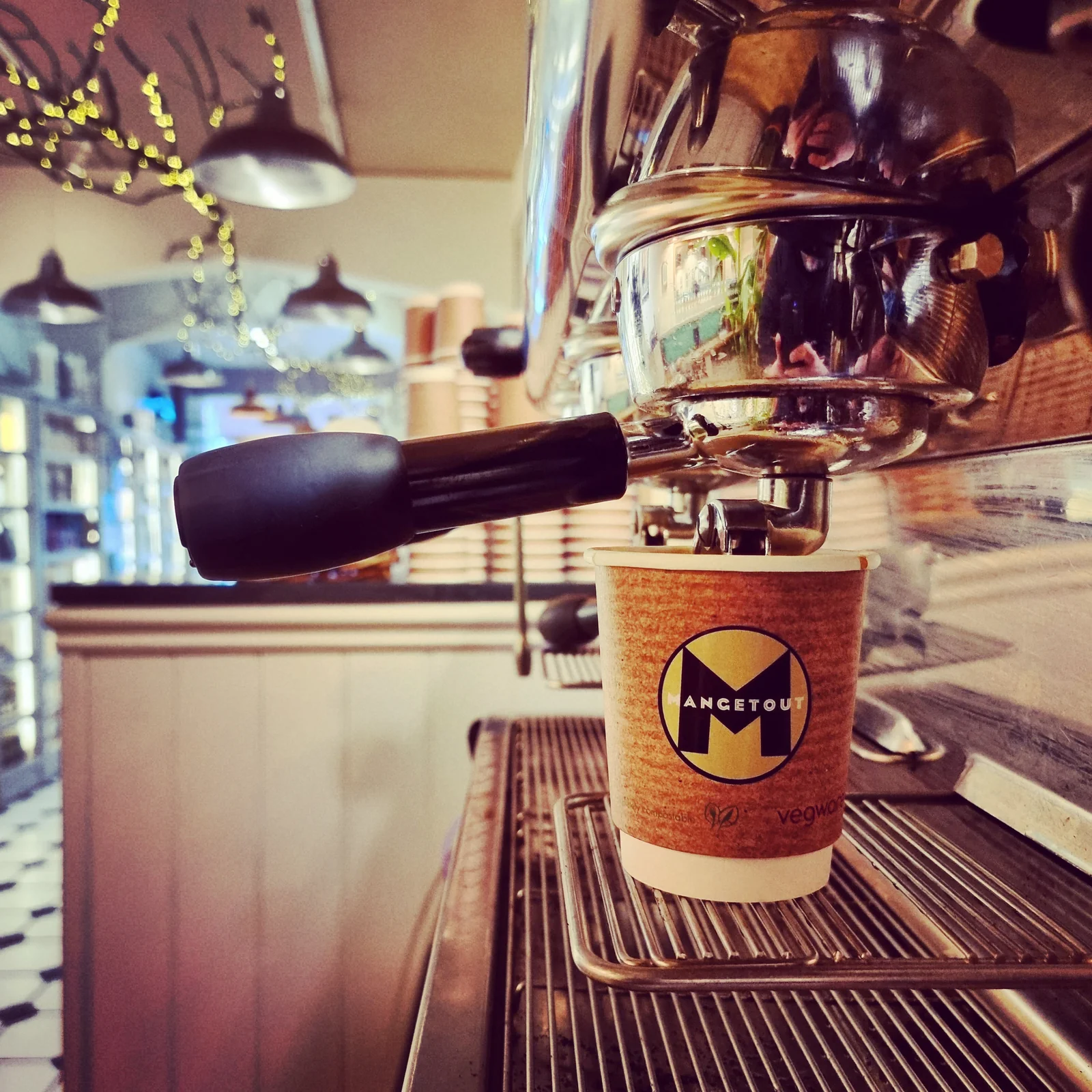 A branded Mangetout takeaway coffee beside an espresso machine