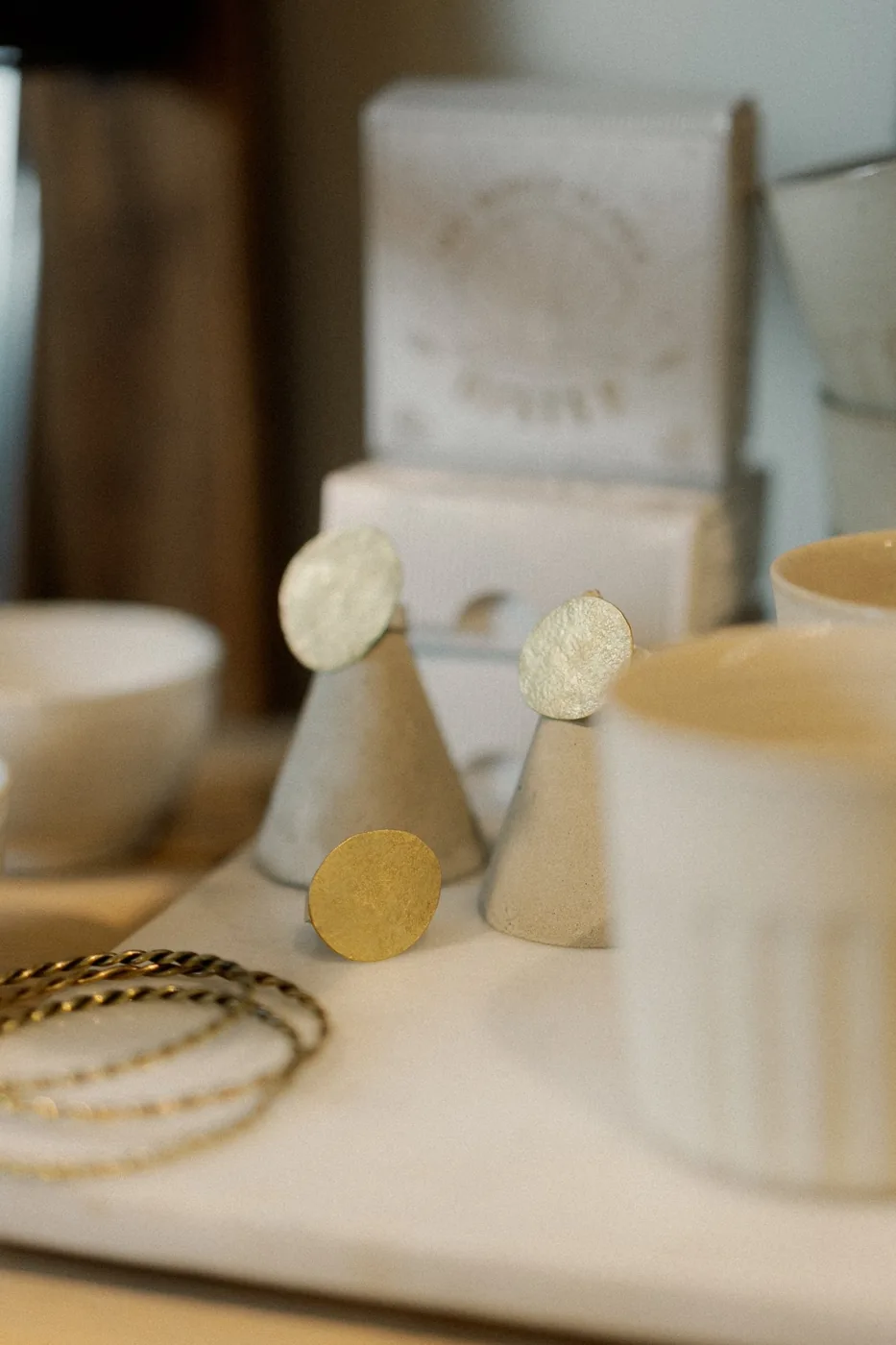 Gold earrings on display beside ceramics at Me and East